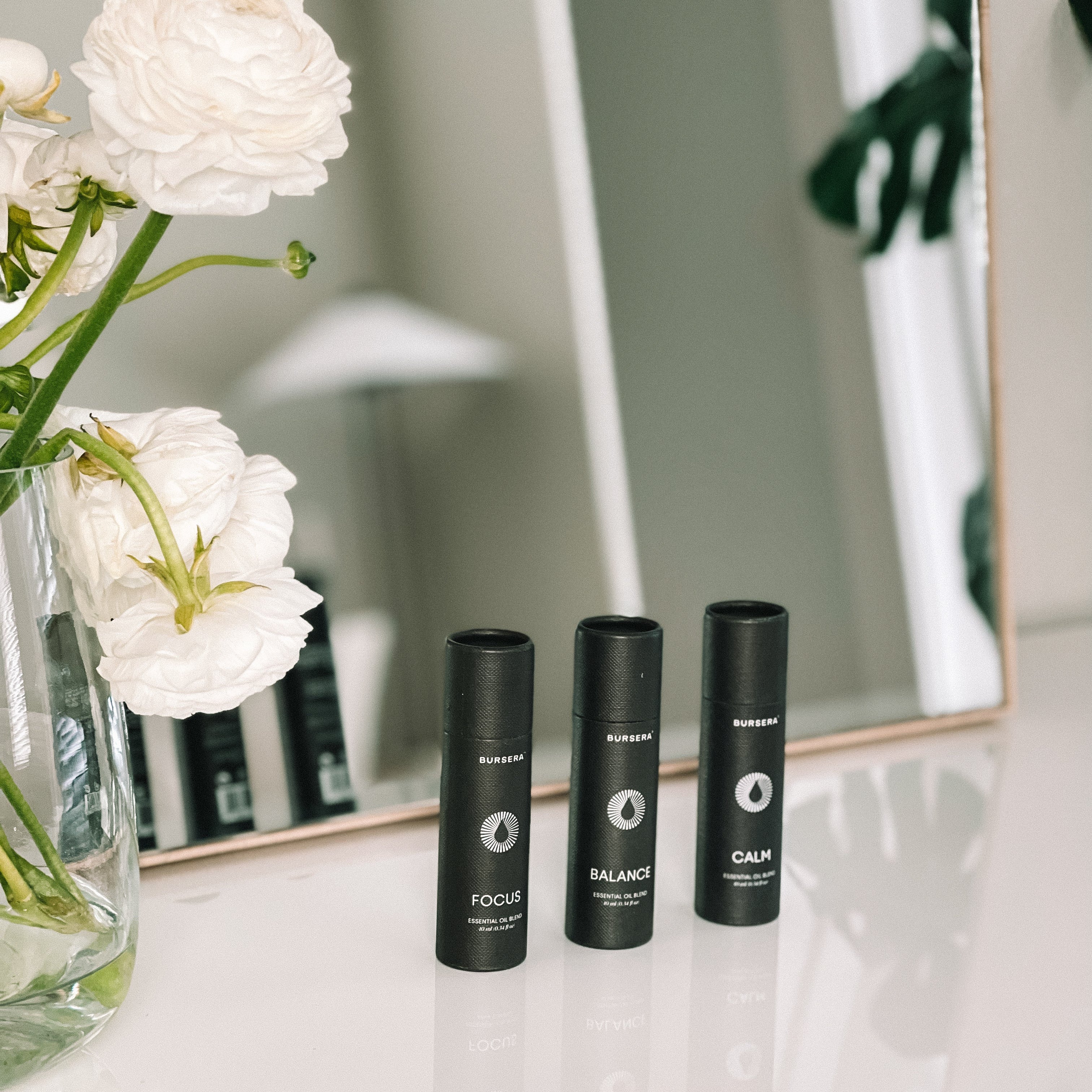 Three black bottles labeled 'Focus', 'Balance', and 'Calm' on a surface with white flowers in the foreground.
