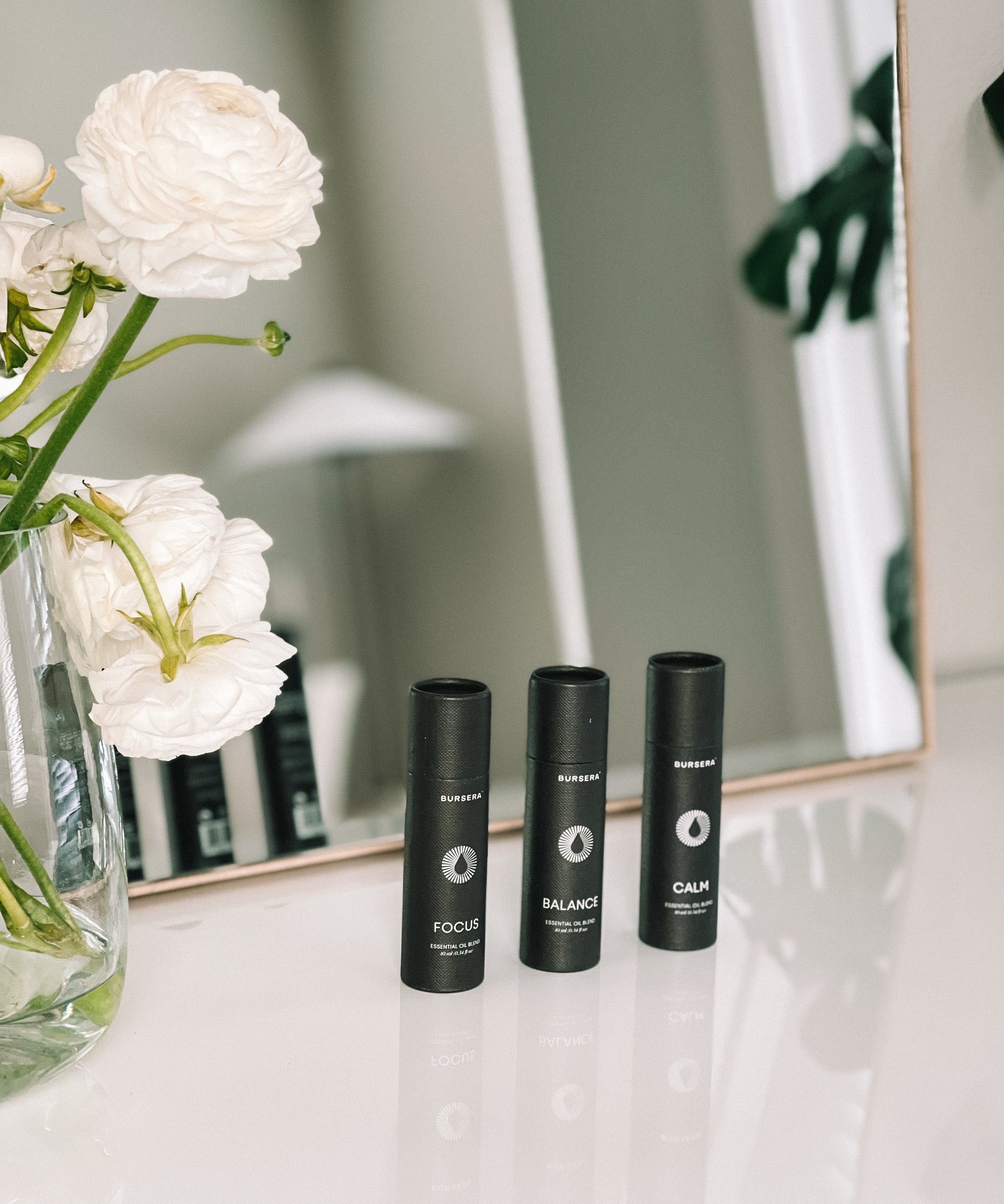 Three black bottles labeled 'Focus', 'Balance', and 'Calm' on a surface with white flowers in the foreground.