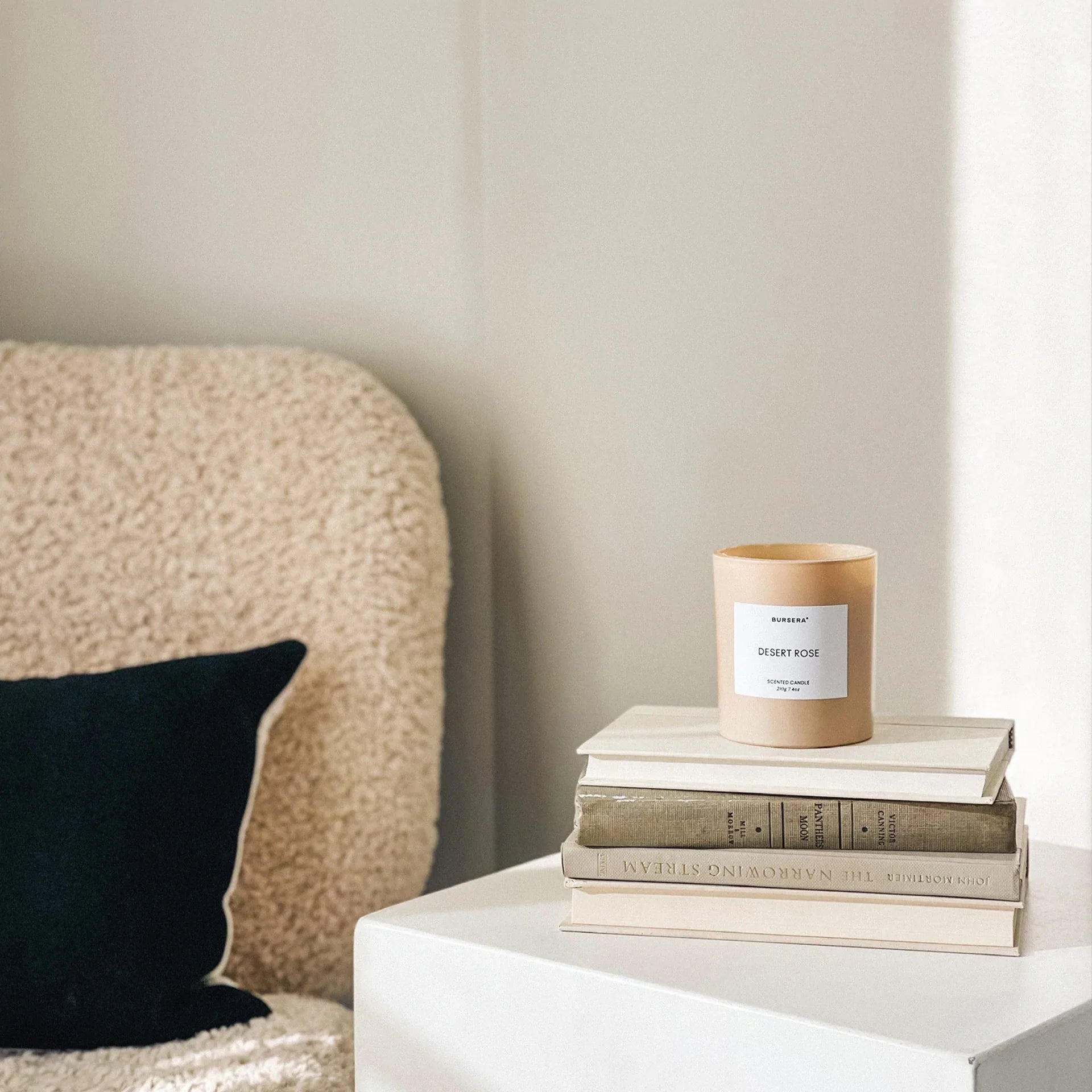 Candle on a stack of books next to a textured headboard and black pillow.