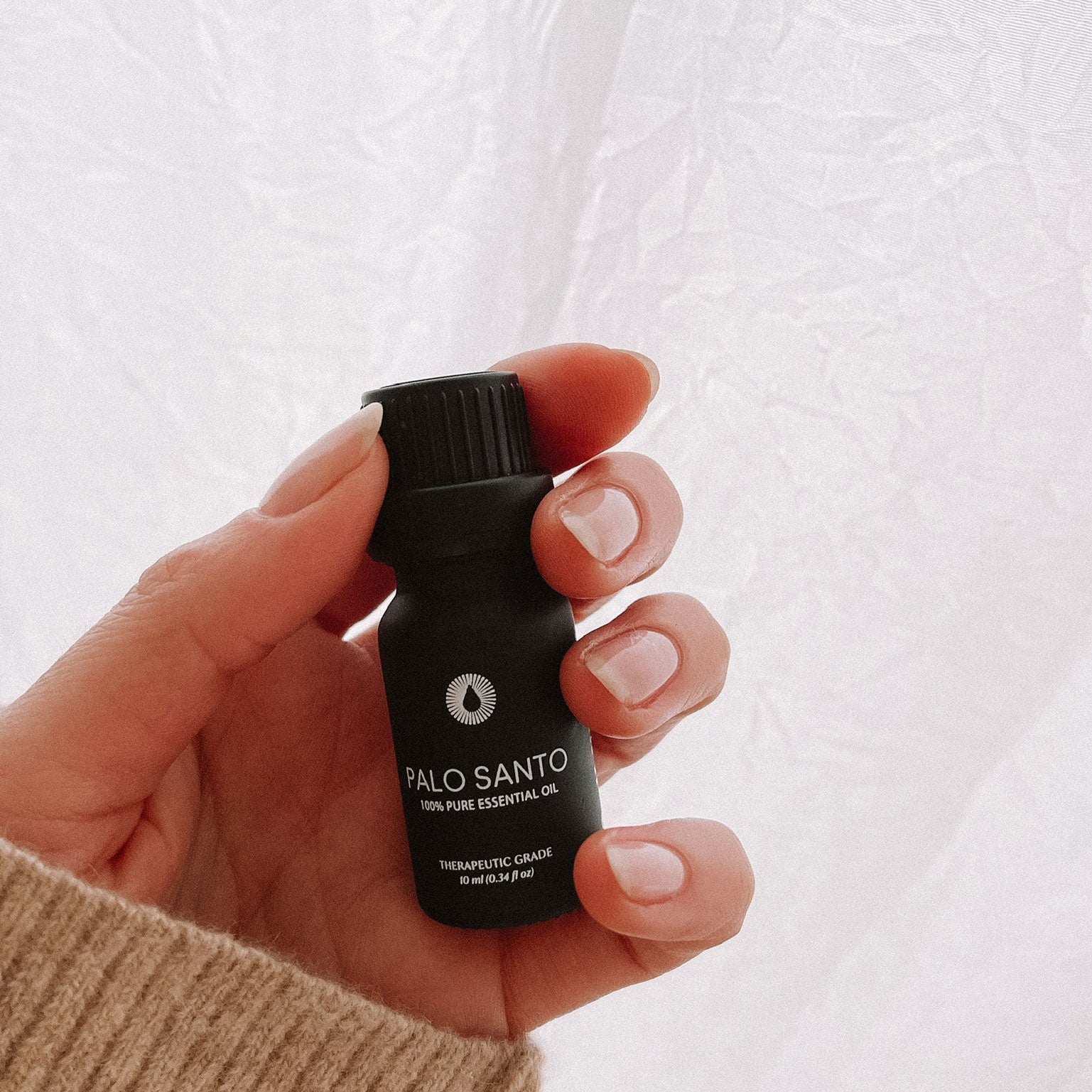 Hand holding a black Palo Santo essential oil bottle against a white background