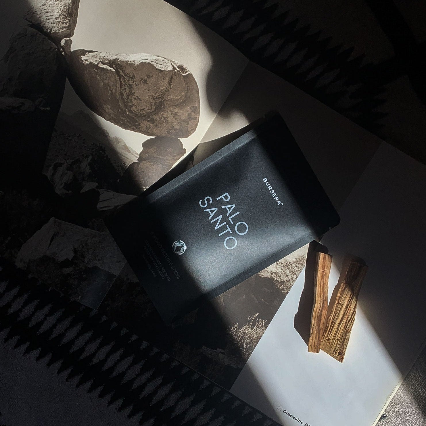Black Palo Santo perfume bottle on a magazine with rocks and sticks