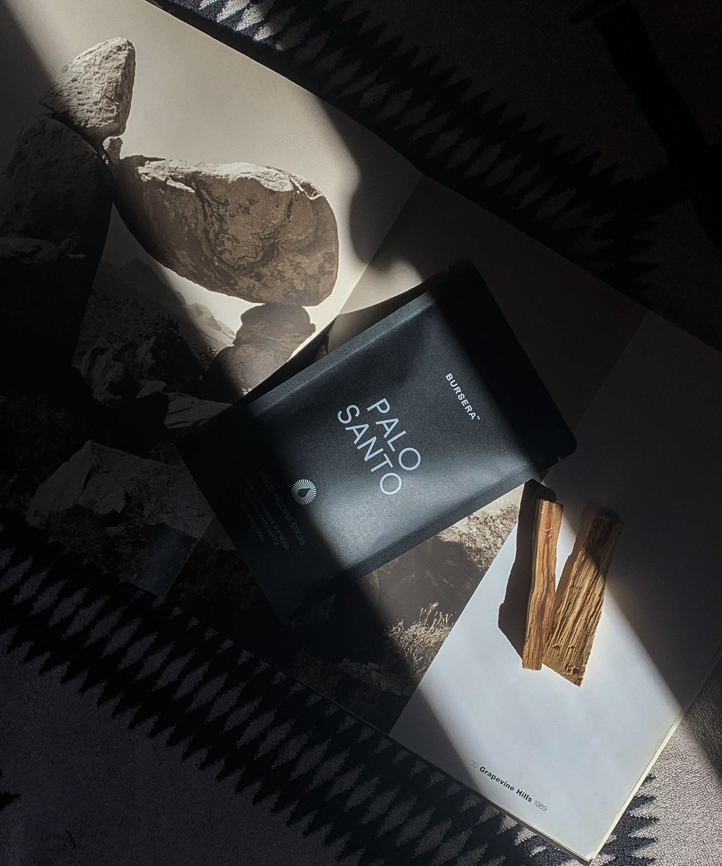 Black Palo Santo perfume bottle on a magazine with rocks and sticks