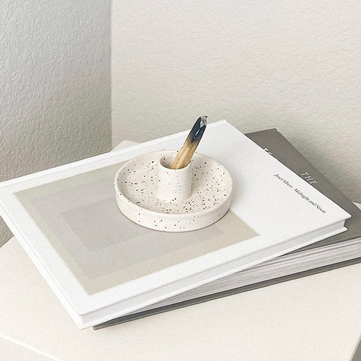 Small speckled ceramic dish with a wooden stick on top of a stack of books.