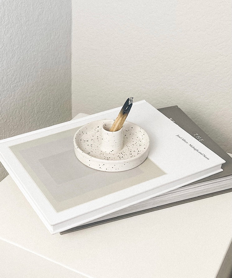Small speckled ceramic dish with a wooden stick on top of a stack of books.