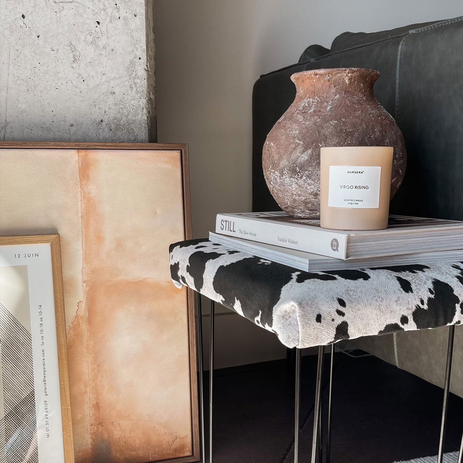 Decorative setup with a candle, vase, and books on a stool against a wall.