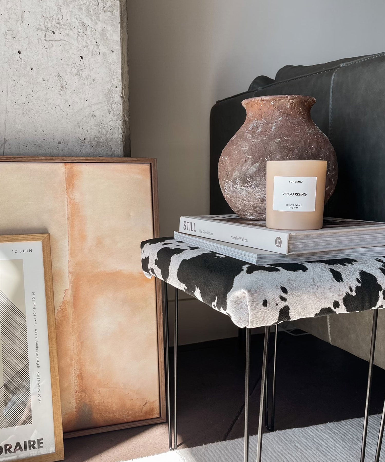 Decorative setup with a candle, vase, and books on a stool against a wall.