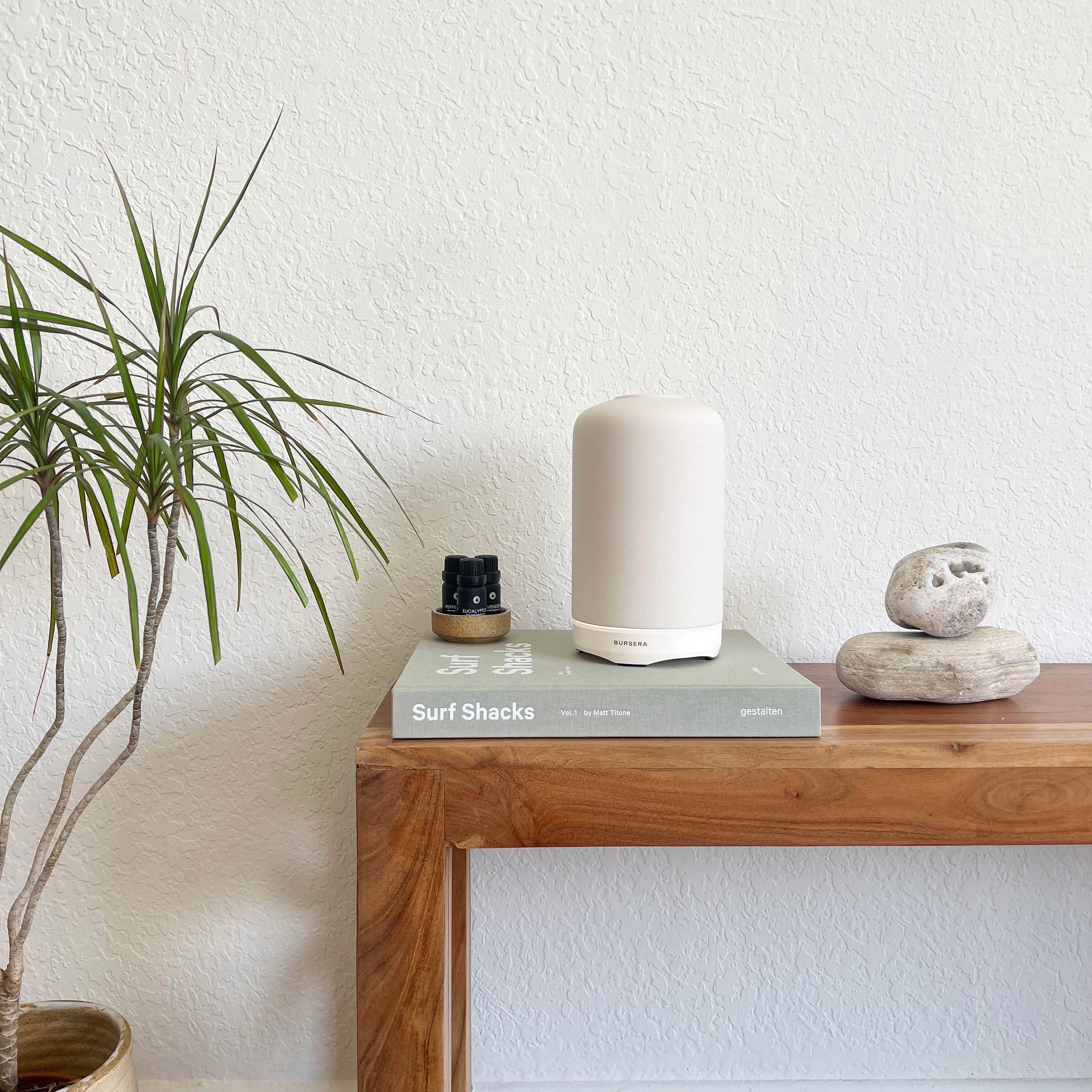 White diffuser on a wooden table with a plant and books in the background