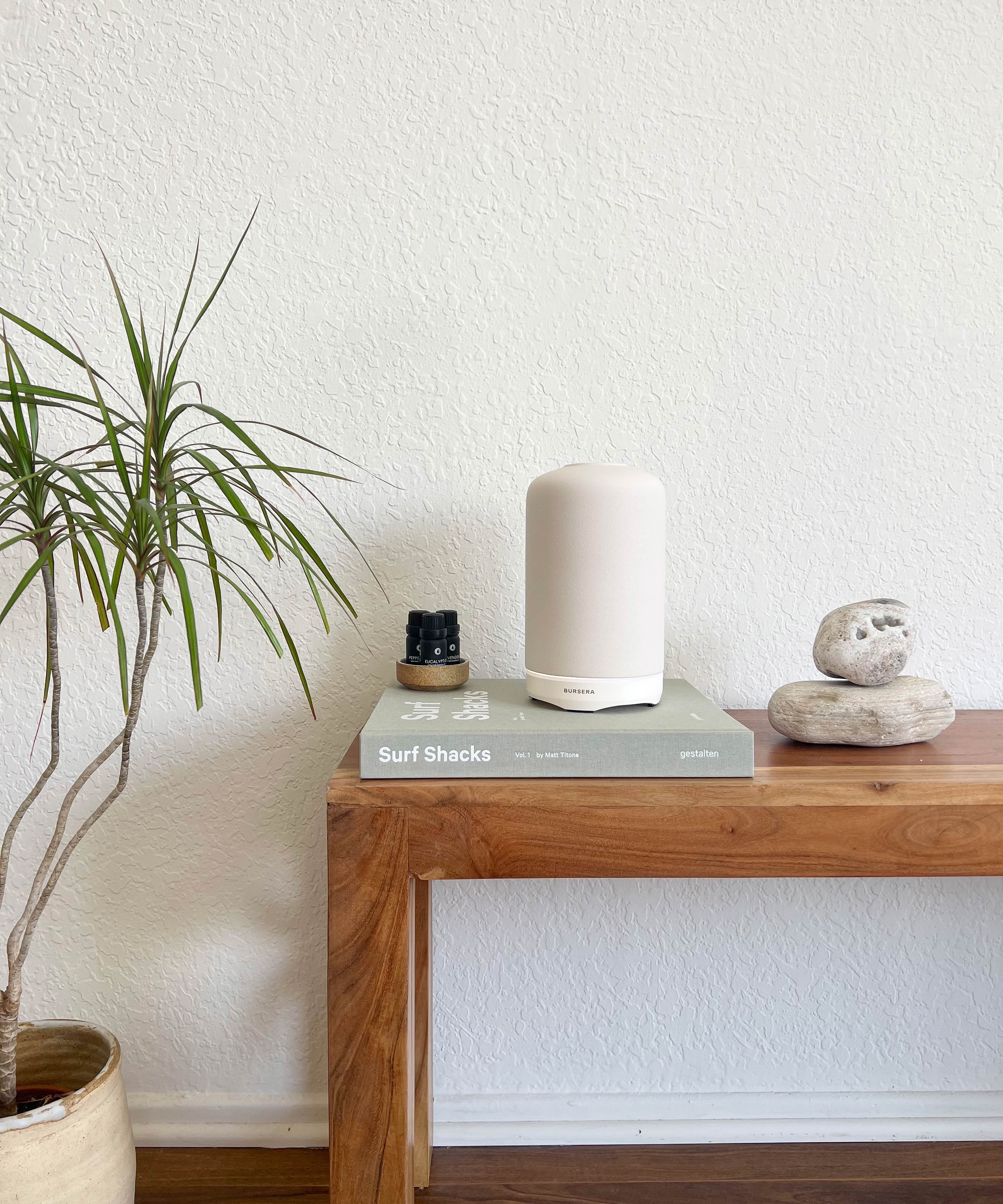 White diffuser on a wooden table with a plant and books in the background