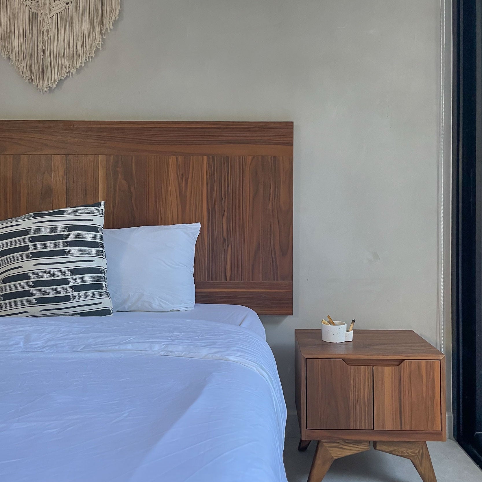 Bedroom with wooden headboard and nightstand against a plain wall.