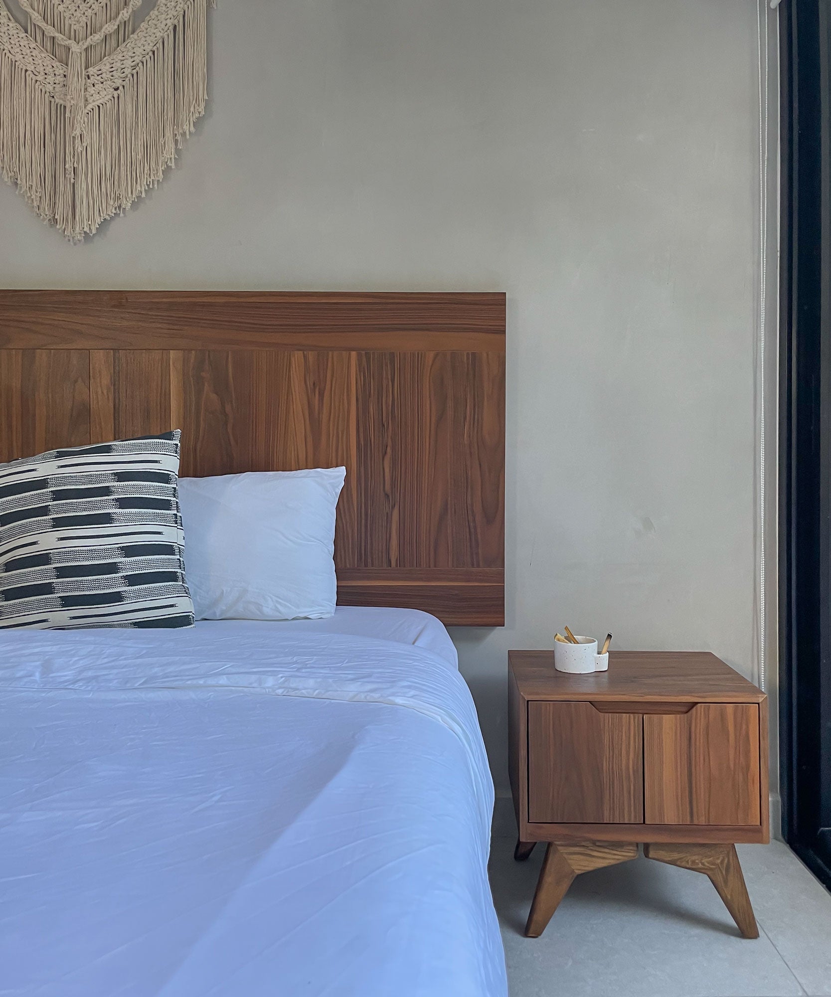 Bedroom with wooden headboard and nightstand against a plain wall.