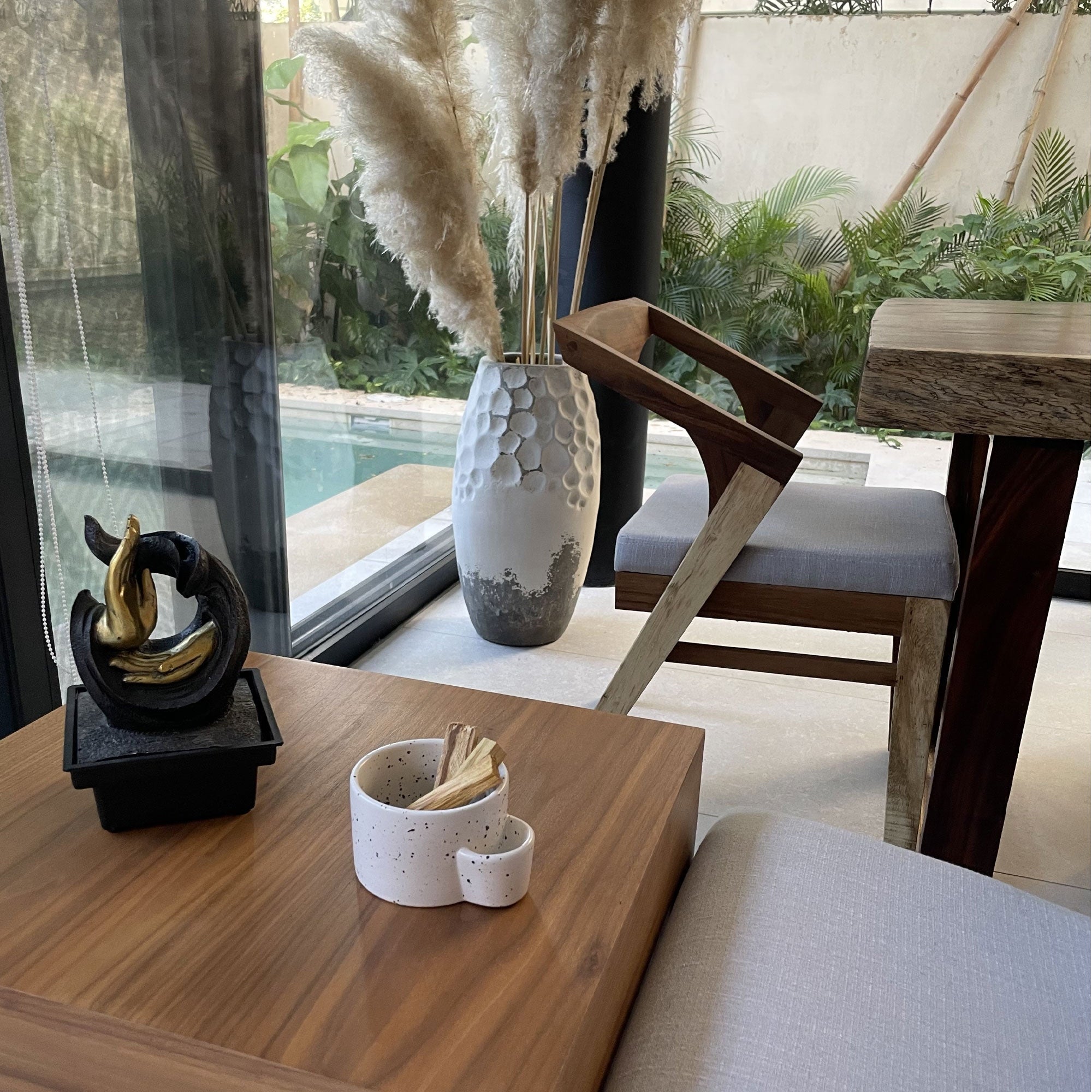 Decorative elements on a wooden table with a view of a pool and outdoor furniture.