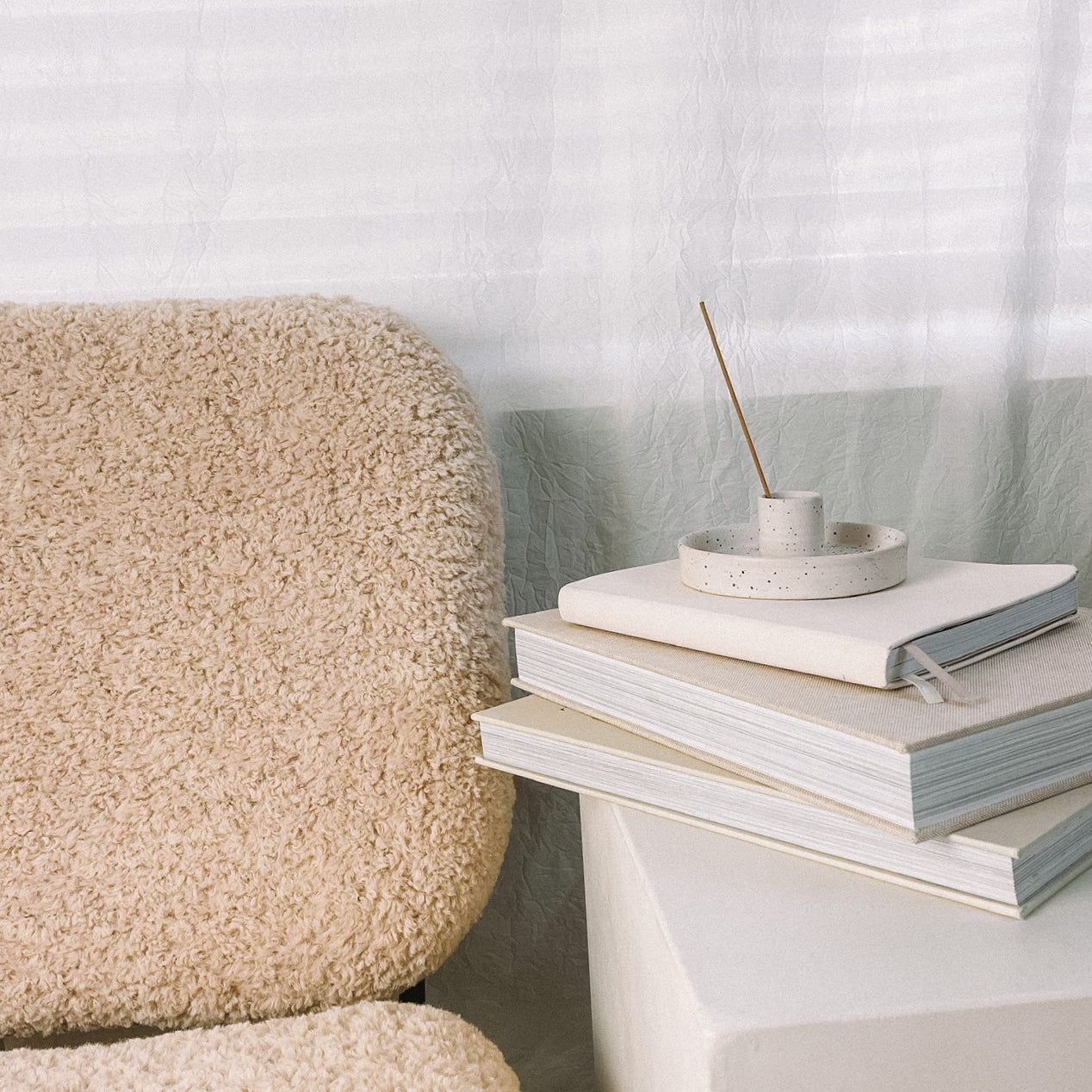 Beige textured chair next to a white table with books and a small plant
