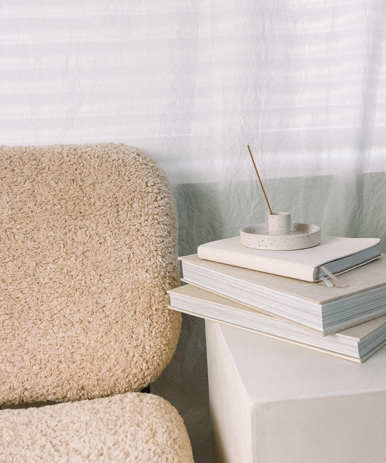 Beige textured chair next to a white table with books and a small plant