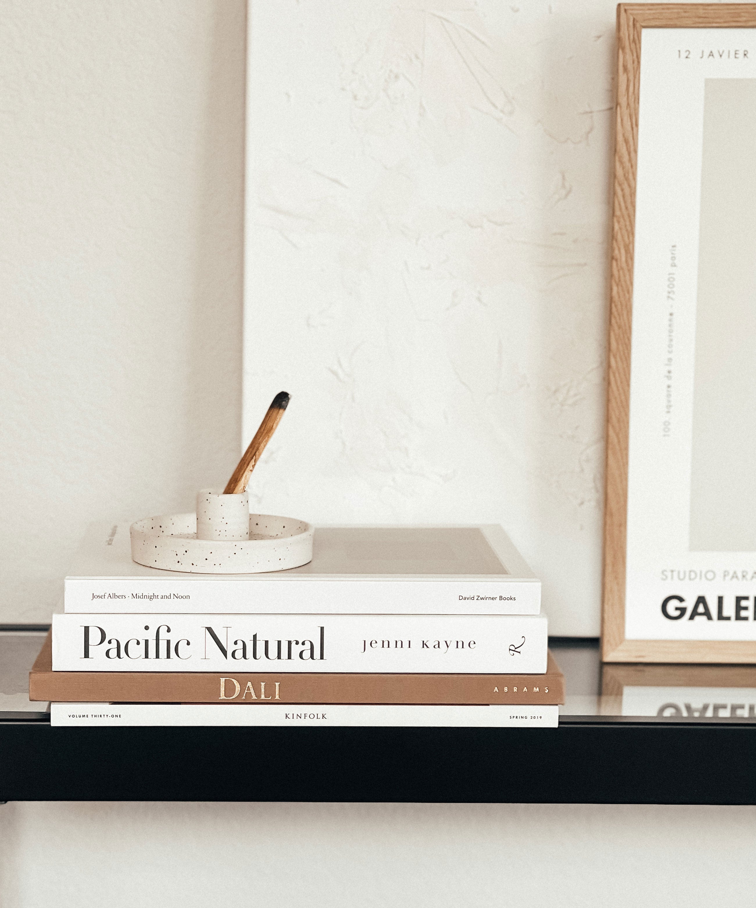 Stack of books on a shelf with a framed picture in the background