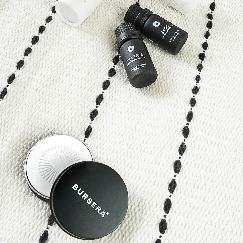 Two black bottles and a compact with 'Bursera' branding on a textured white surface.