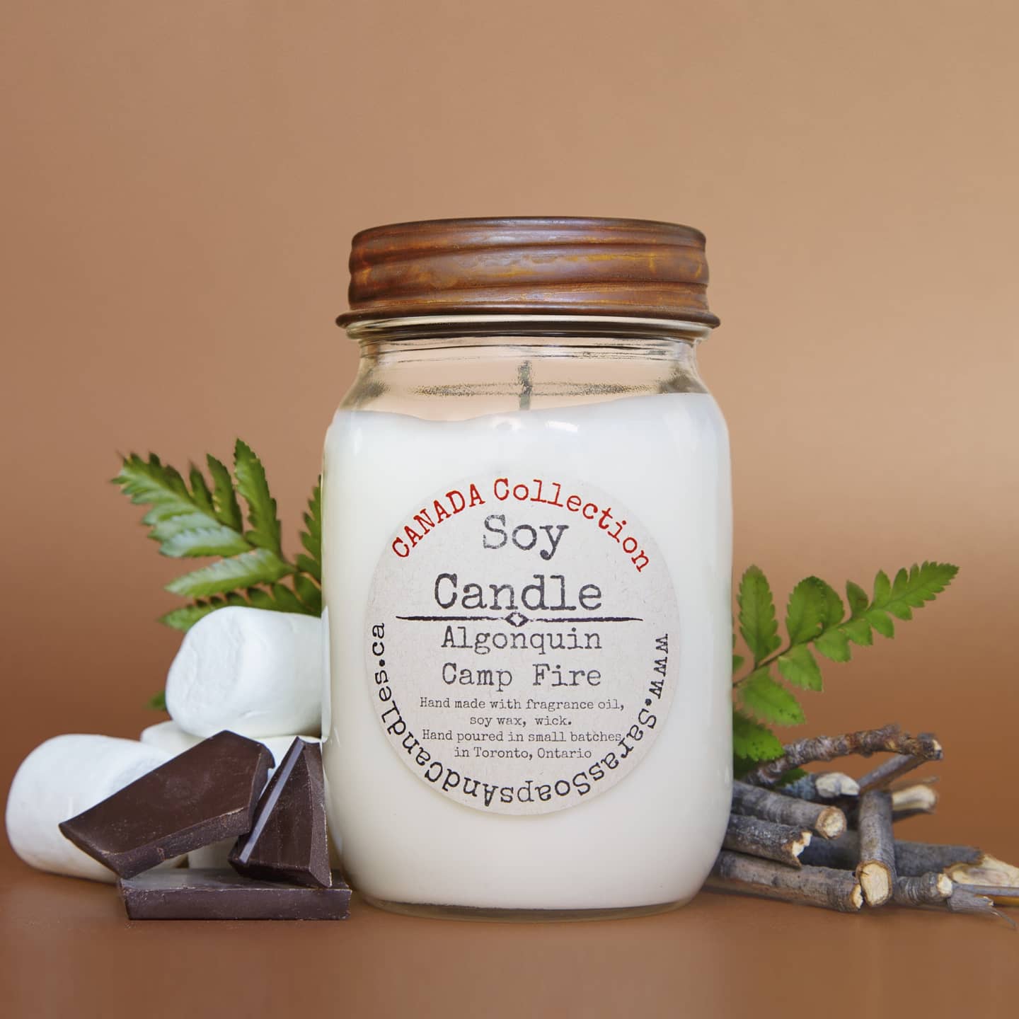 Soy candle labeled 'Canada Collection' with marshmallows, chocolate, and twigs on a brown background from Stop and Smell the Candles
