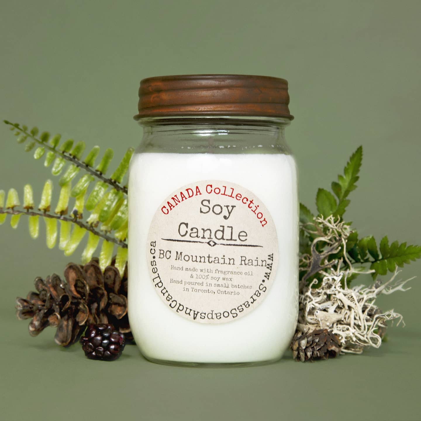 Jar candle labeled 'Canada Collection Soy Candle' with decorative elements on a green background