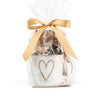 Gift basket with a white bag featuring a heart design, filled with snacks, and tied with a gold ribbon on a white background.