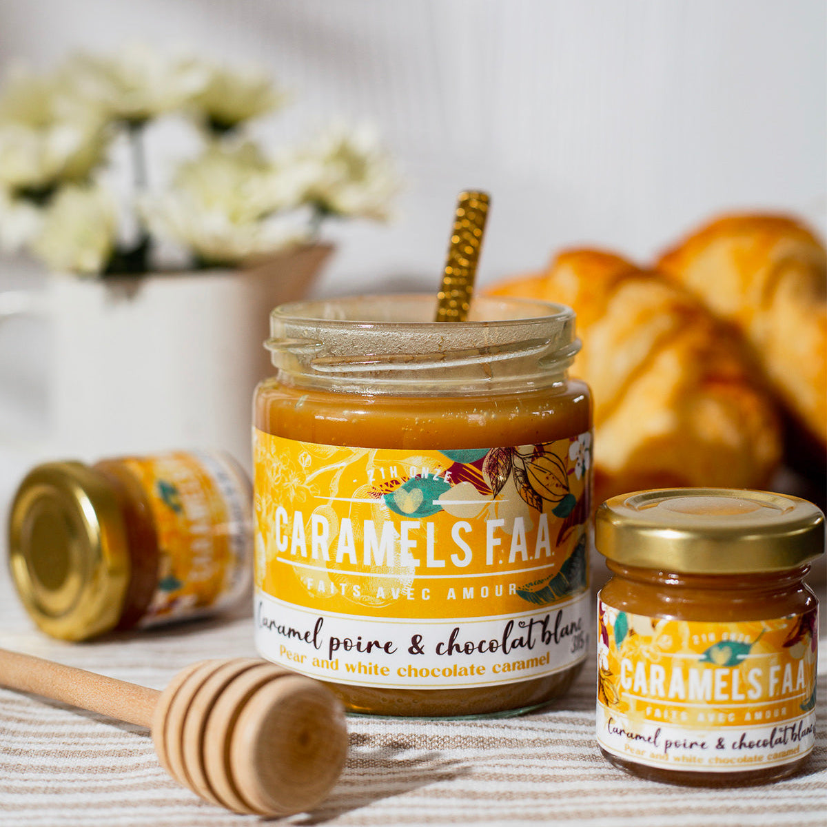 Jar of Caramels FAA with a honey dipper on a table with flowers and pastries in the background