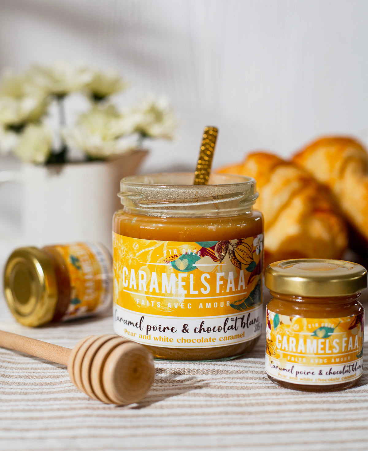 Jar of Caramels FAA with a honey dipper on a table with flowers and pastries in the background