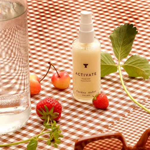 Cardea Auset 'Activate' mood mist on a checkered tablecloth with strawberries and cherries.