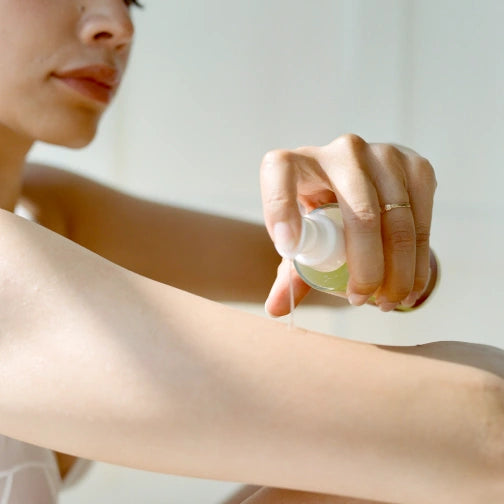Person applying Cardea AuSet Golden Hour Body oil to their arm with a neutral background