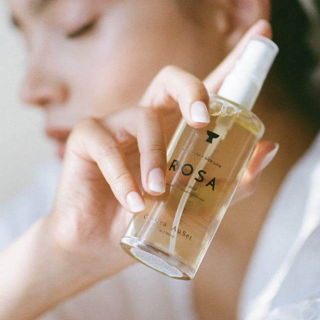 Hand holding a clear bottle labeled 'Rosa' with a blurred background