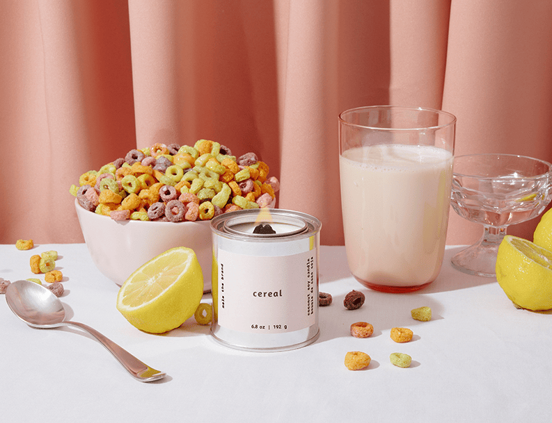 Cereal bowl with colorful cereal, a glass of milk, and a container labeled 'cereal' on a white surface with pink curtains in the background.
