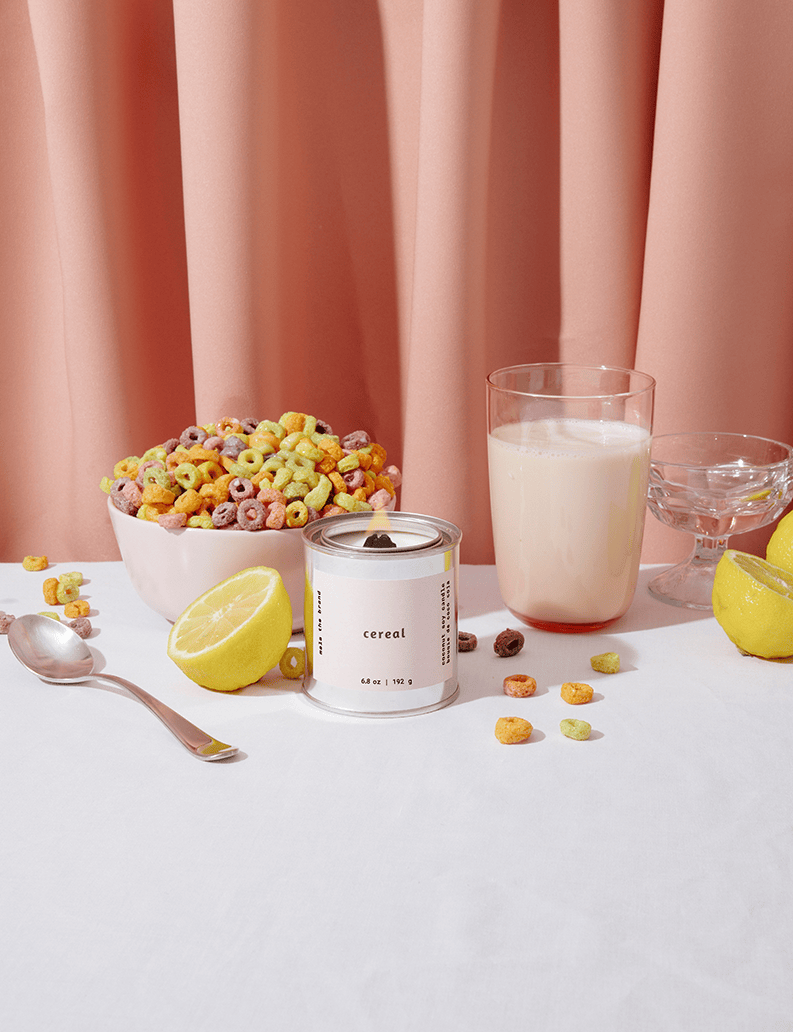 Cereal bowl with colorful cereal, a glass of milk, and a container labeled 'cereal' on a white surface with pink curtains in the background.