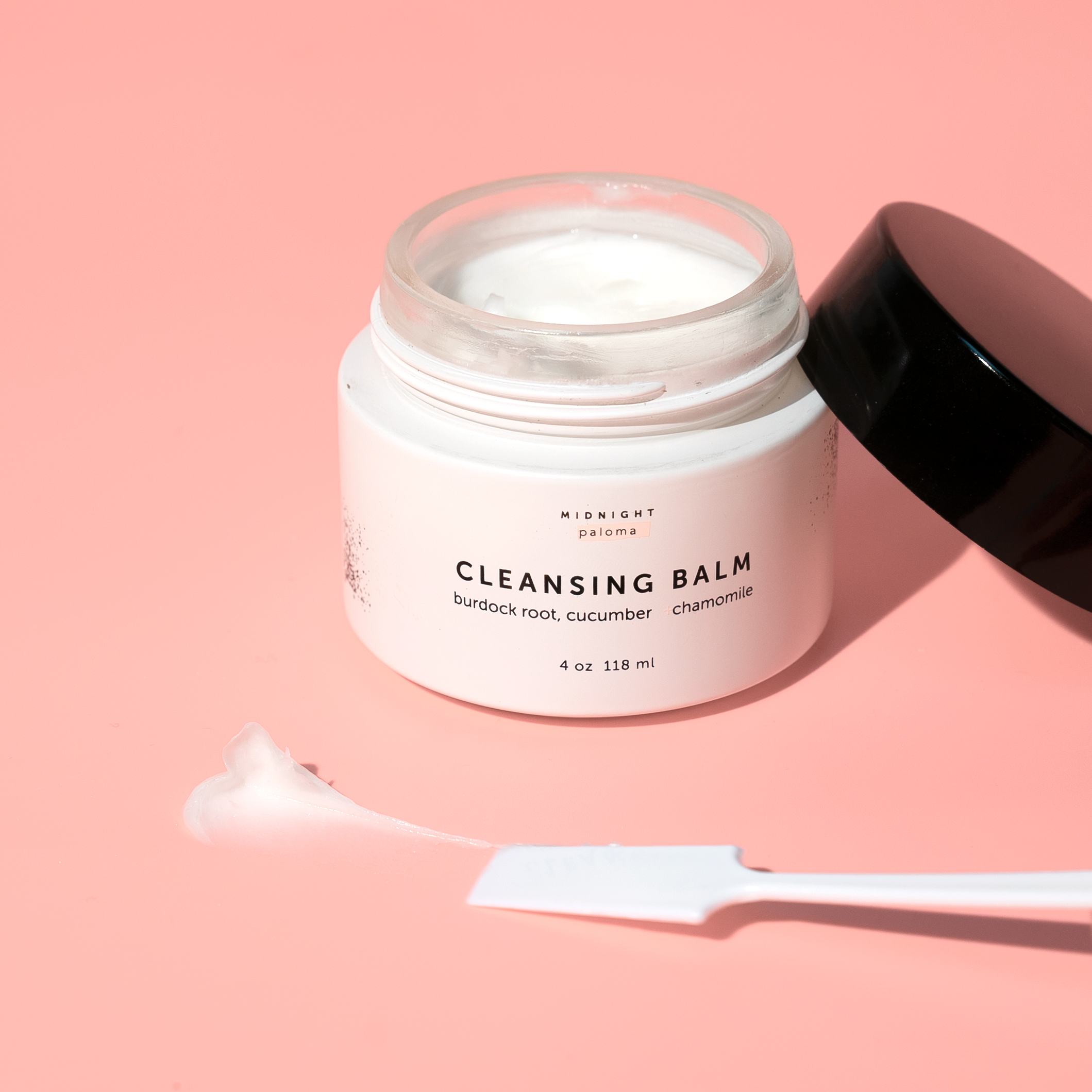 Cleansing balm jar with a spoon on a pink background