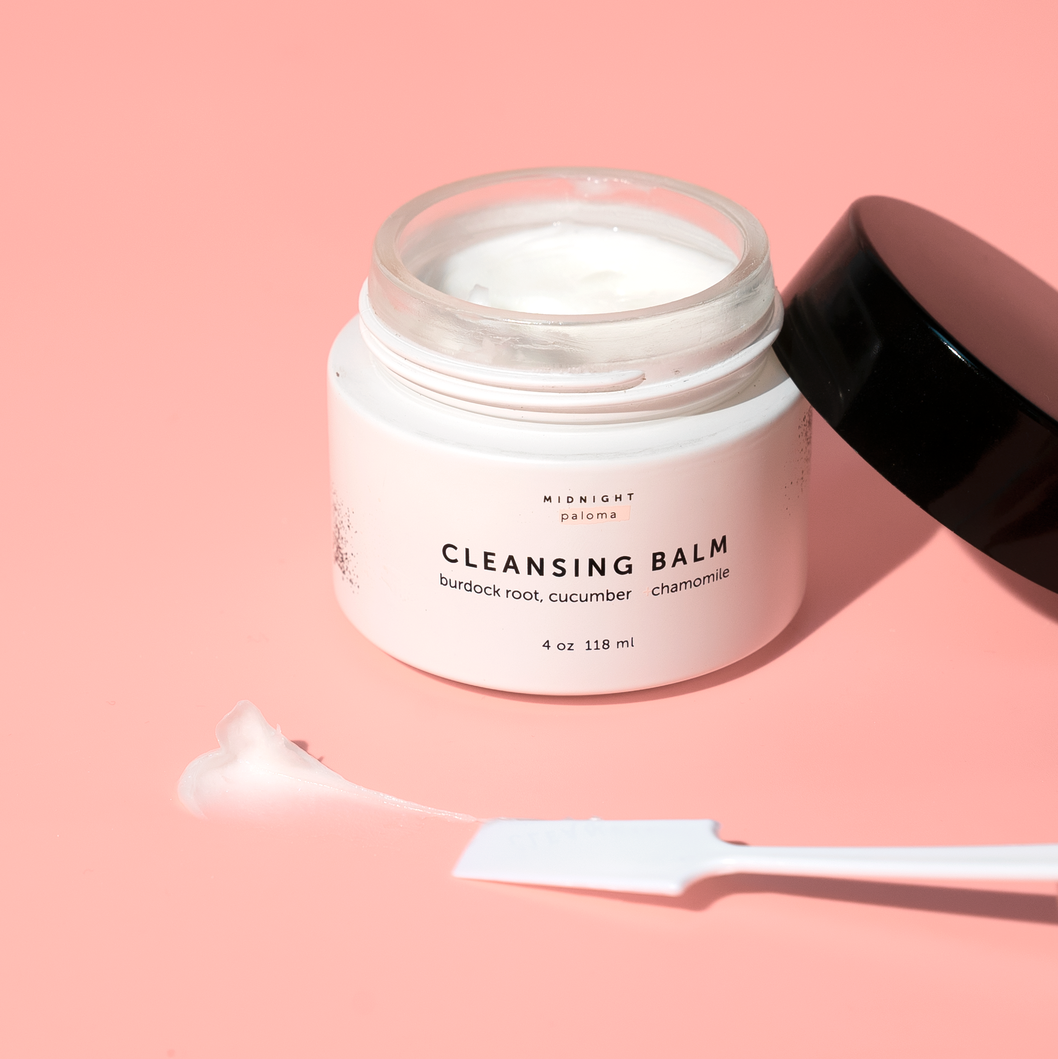 Cleansing balm jar with a spoon on a pink background