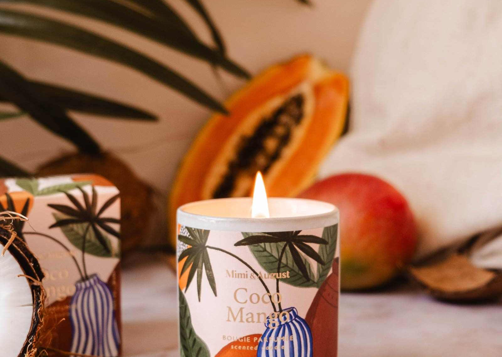 Candle with tropical design surrounded by fruits and leaves on a textured surface