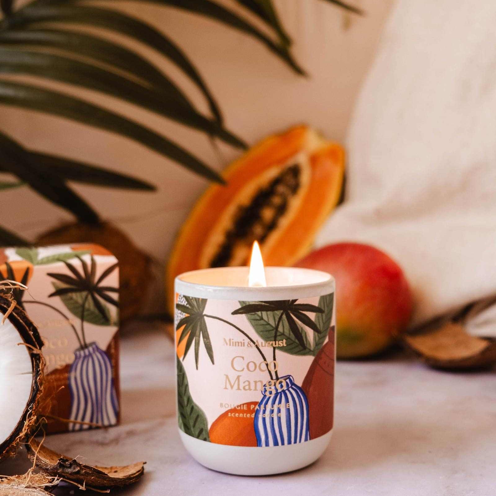 Candle with tropical design surrounded by fruits and leaves on a textured surface