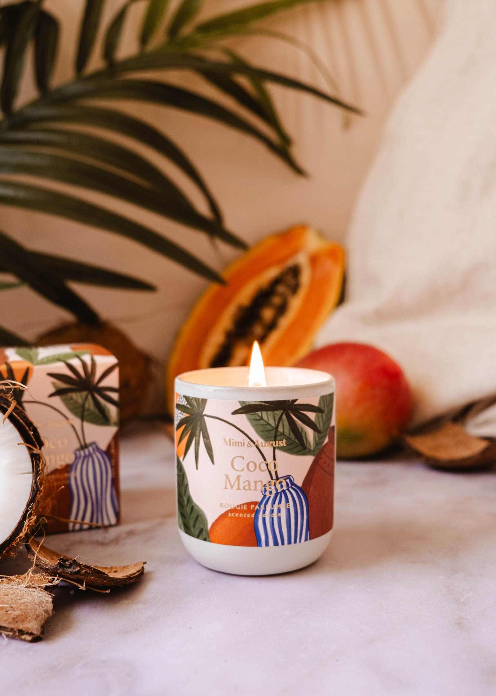 Candle with tropical design surrounded by fruits and leaves on a textured surface
