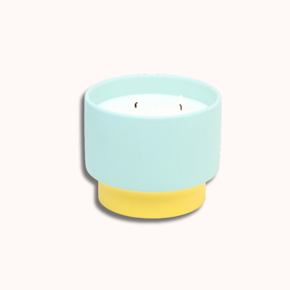 Candle in a light blue holder with a yellow base on a white background
