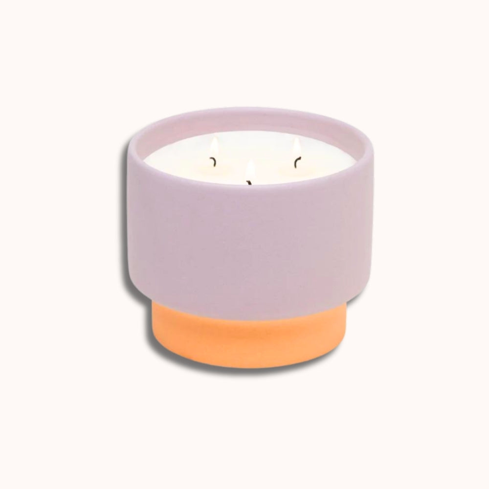 Candle in a two-toned lavender and orange pot on a white background