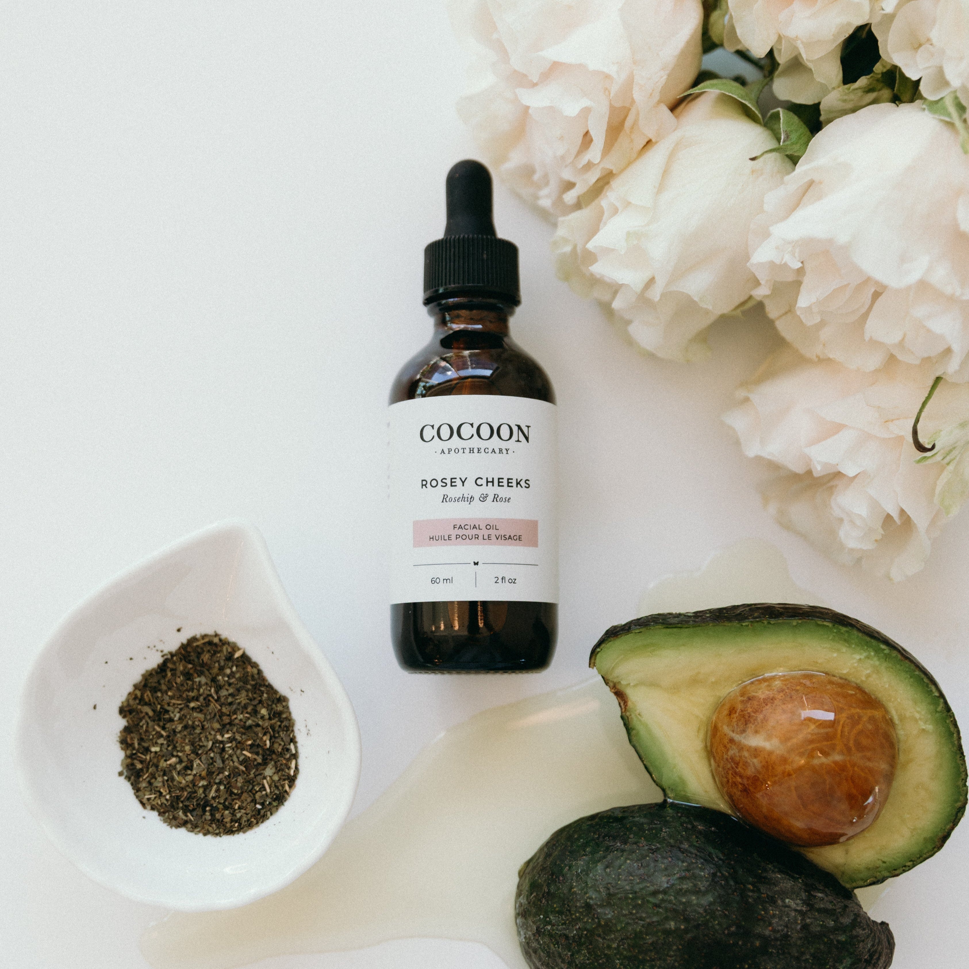 Cocoon skincare bottle with avocado, flowers, and a spoon on a white background