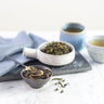 Tea leaves in a bowl with a cup of tea on a marble surface