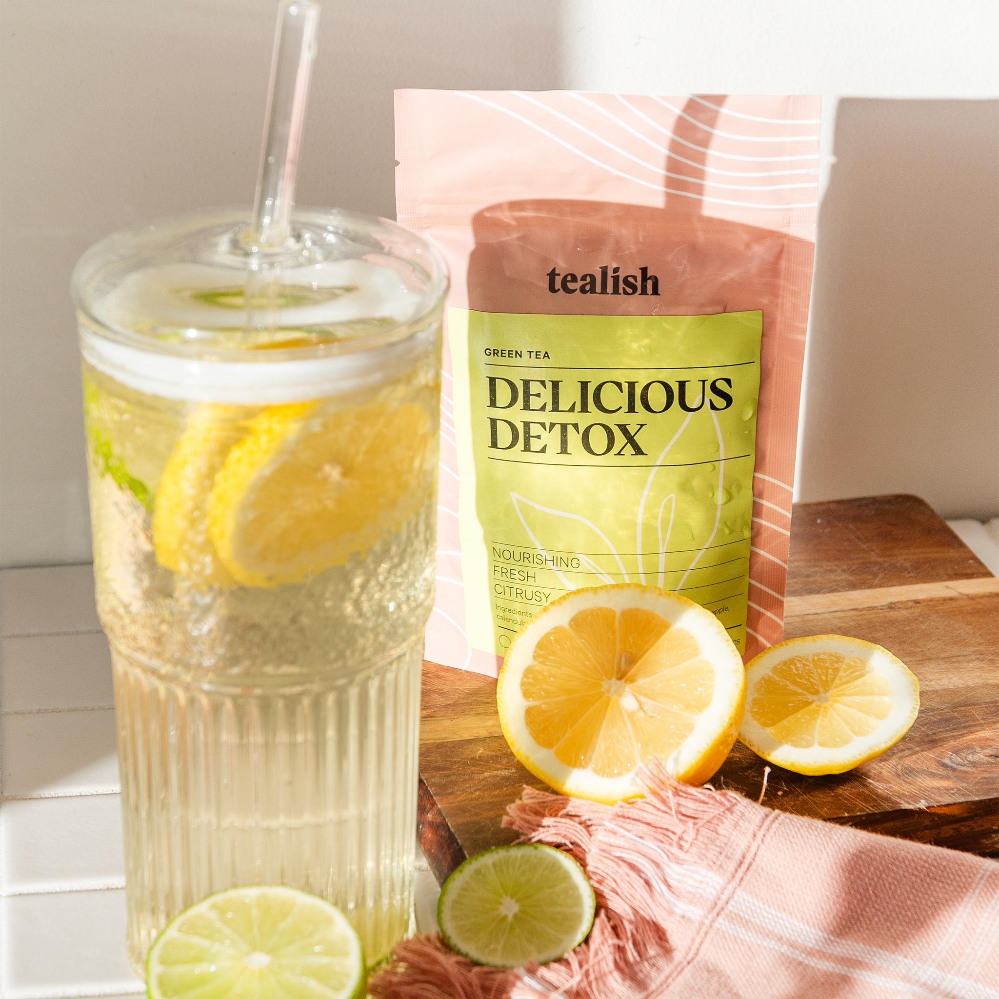 Glass of lemon water with a tealish brand 'Delicious Detox' package on a wooden surface.