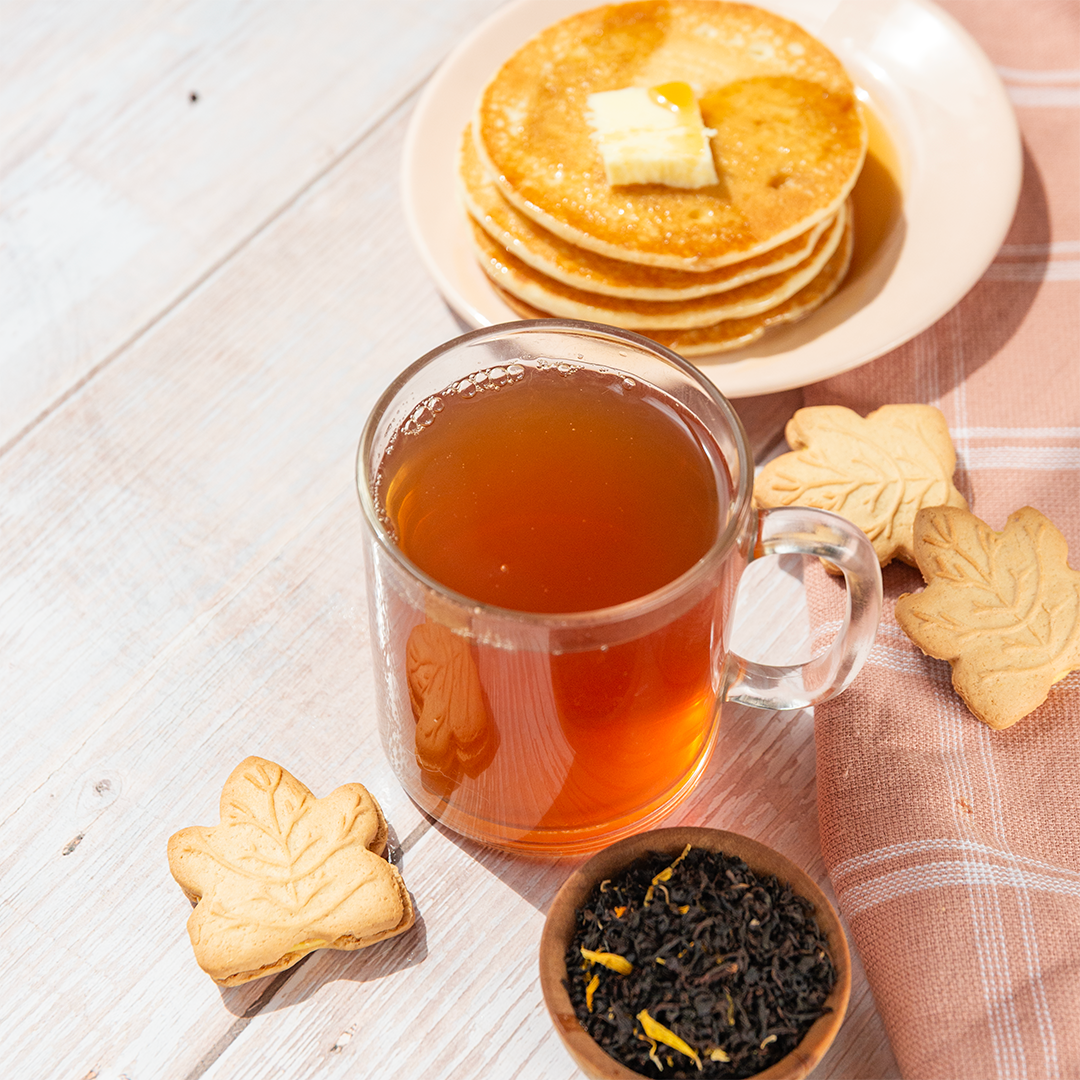 Tea cup with a stack of pancakes and cookies on a wooden surface