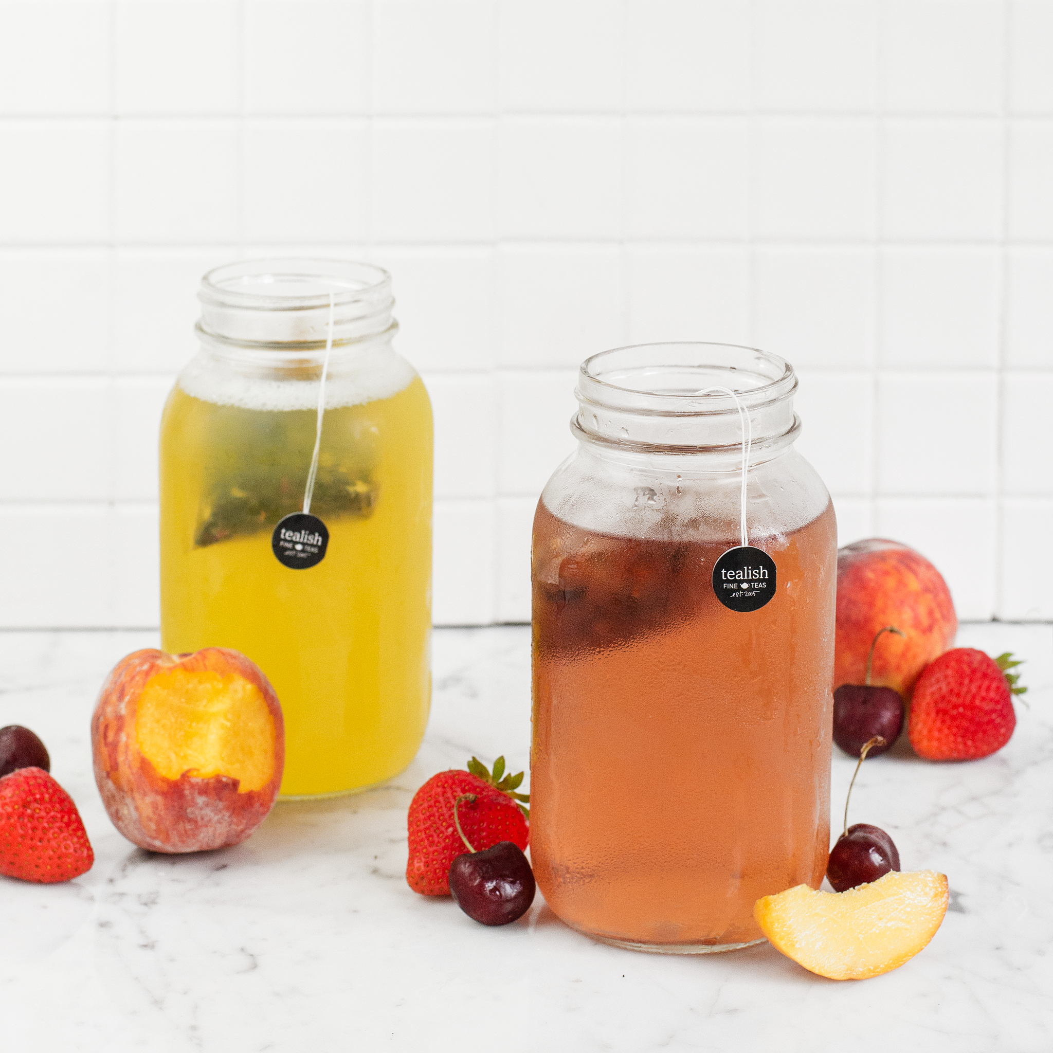 Two jars of iced tea with fruit on a white surface