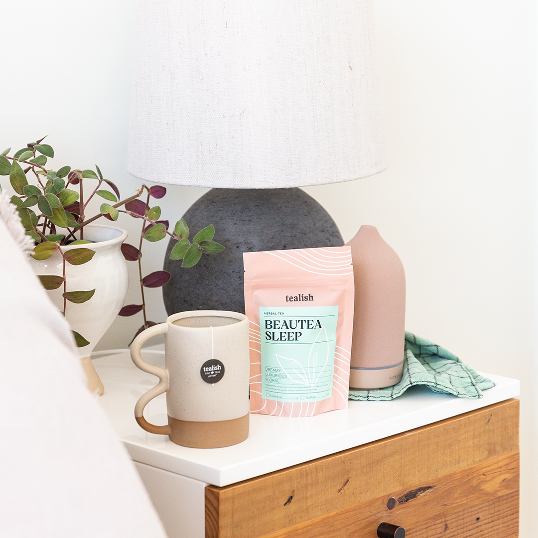 Tea mug and package on a white surface with a plant and wooden drawer in the background