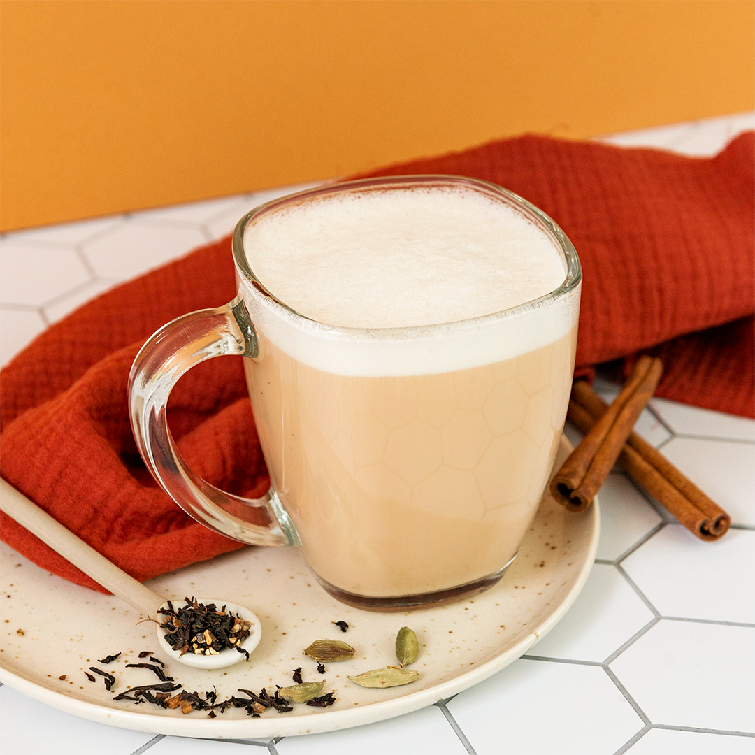 Glass mug of chai tea with spices on a plate against an orange background
