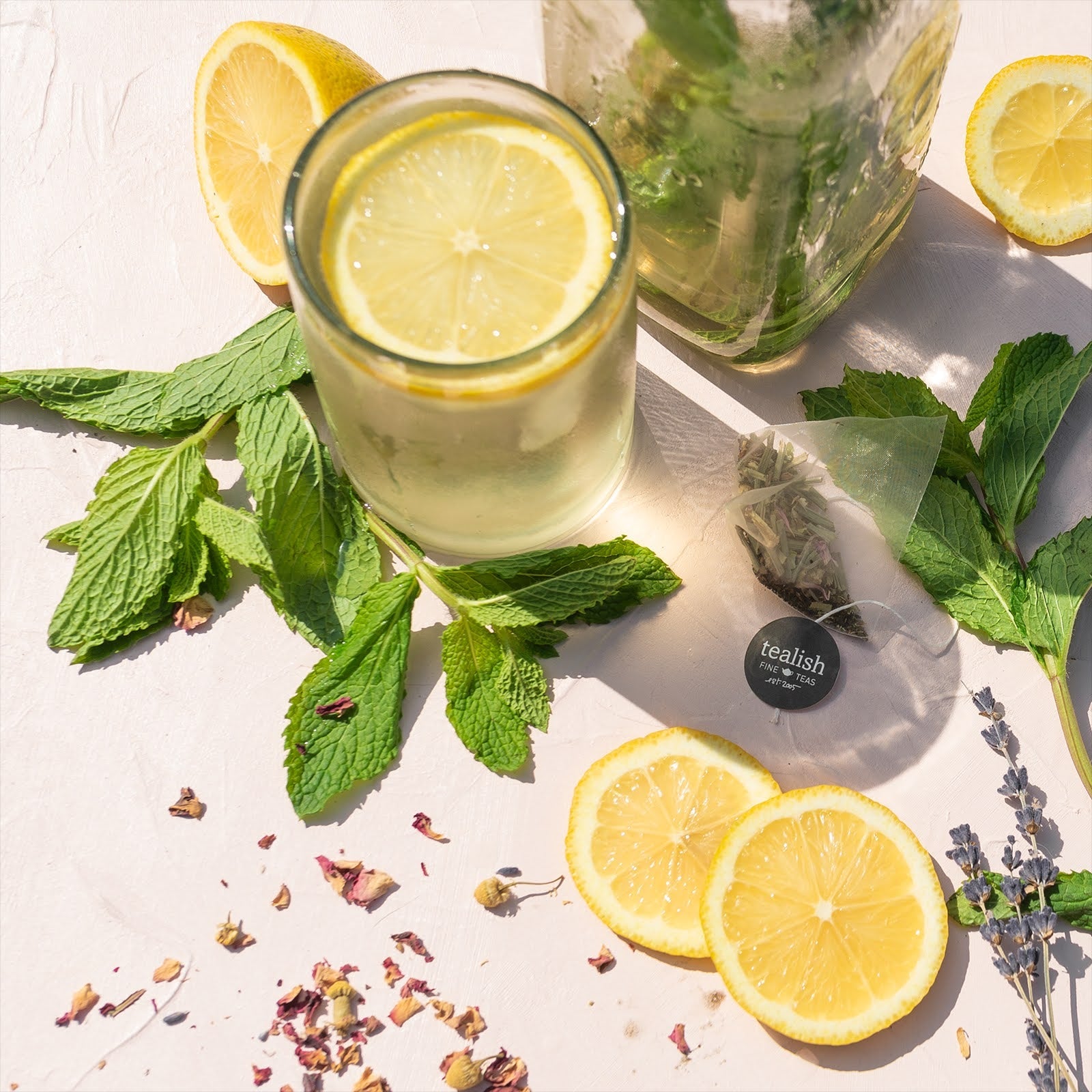 Glass of lemon water with mint leaves and lemon slices on a light surface.