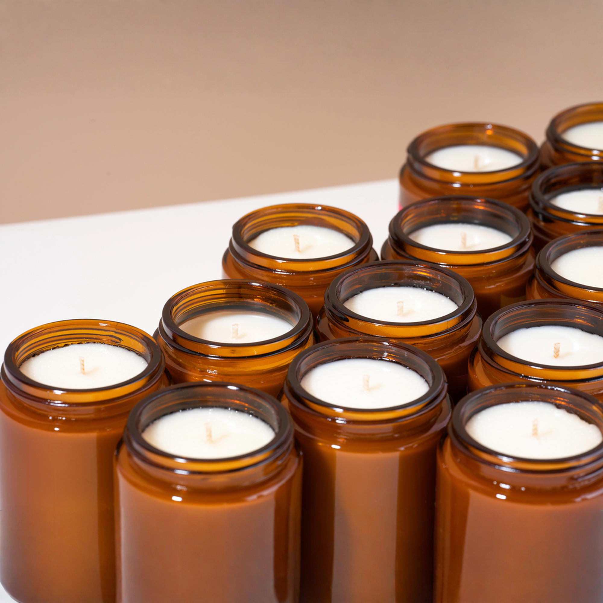 Multiple amber glass jar candles with white wax arranged on a white surface against a warm beige background.