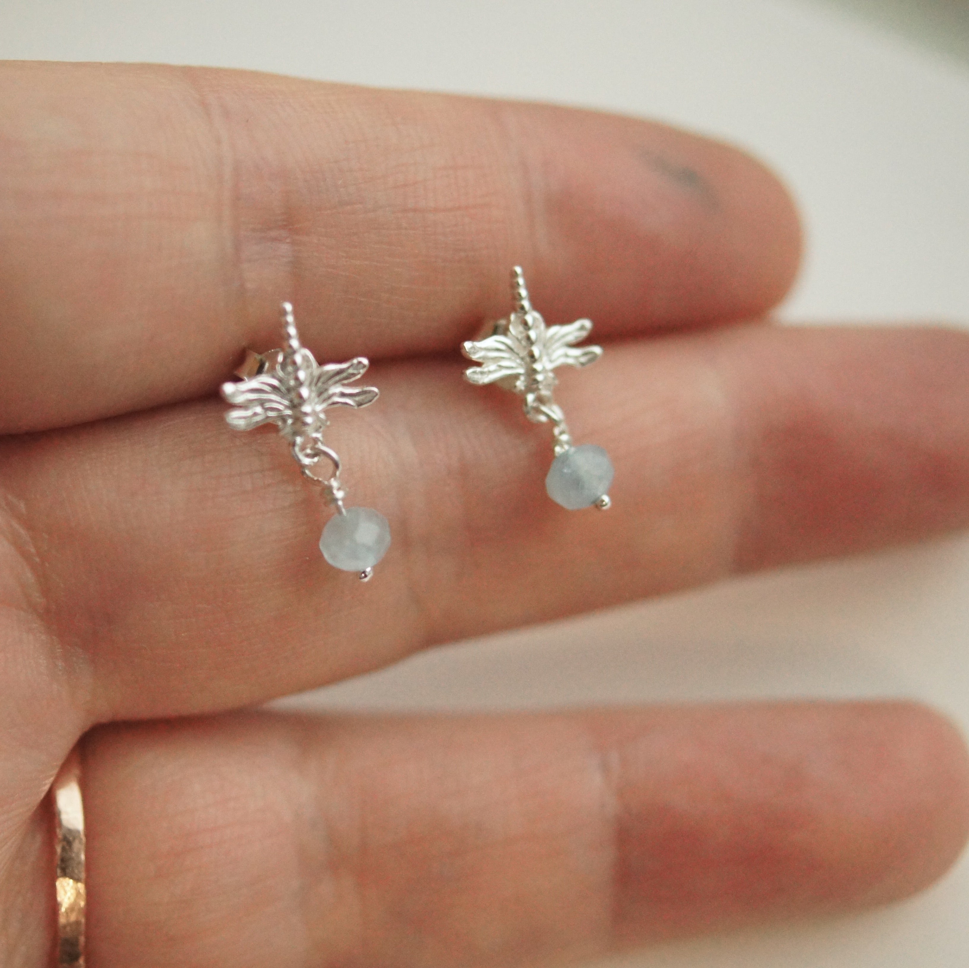 Silver fairy earrings with small beads held between fingers on a light background