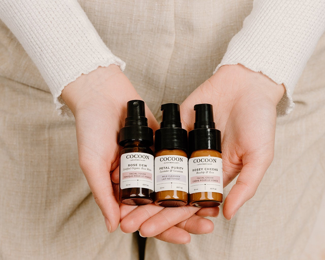 Three bottles of Cocoon skincare products held by a person against a neutral background