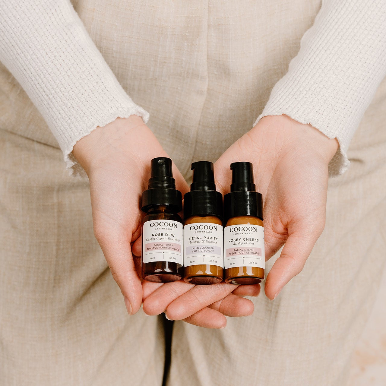 Three bottles of Cocoon skincare products held by a person against a neutral background