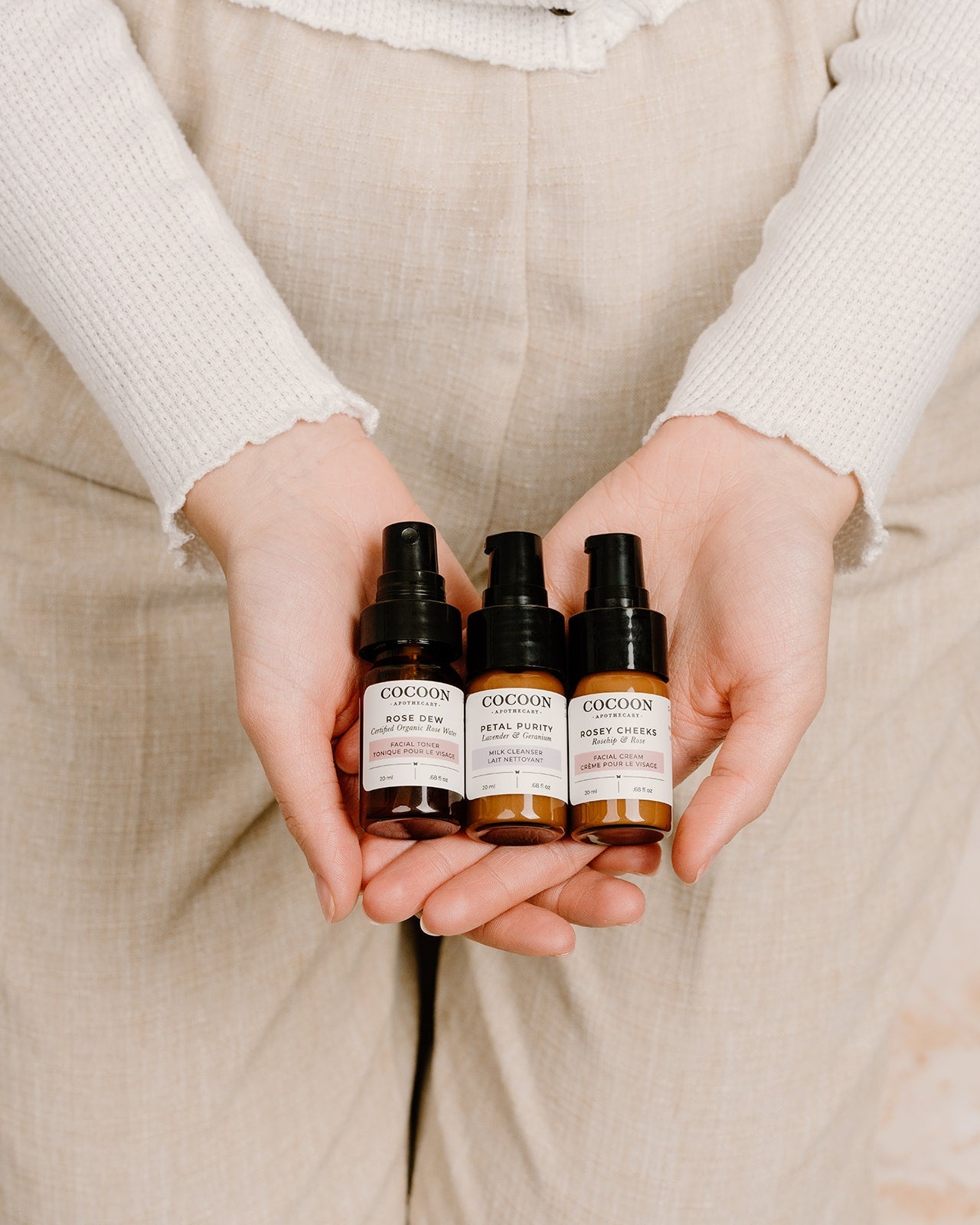 Three bottles of Cocoon skincare products held by a person against a neutral background