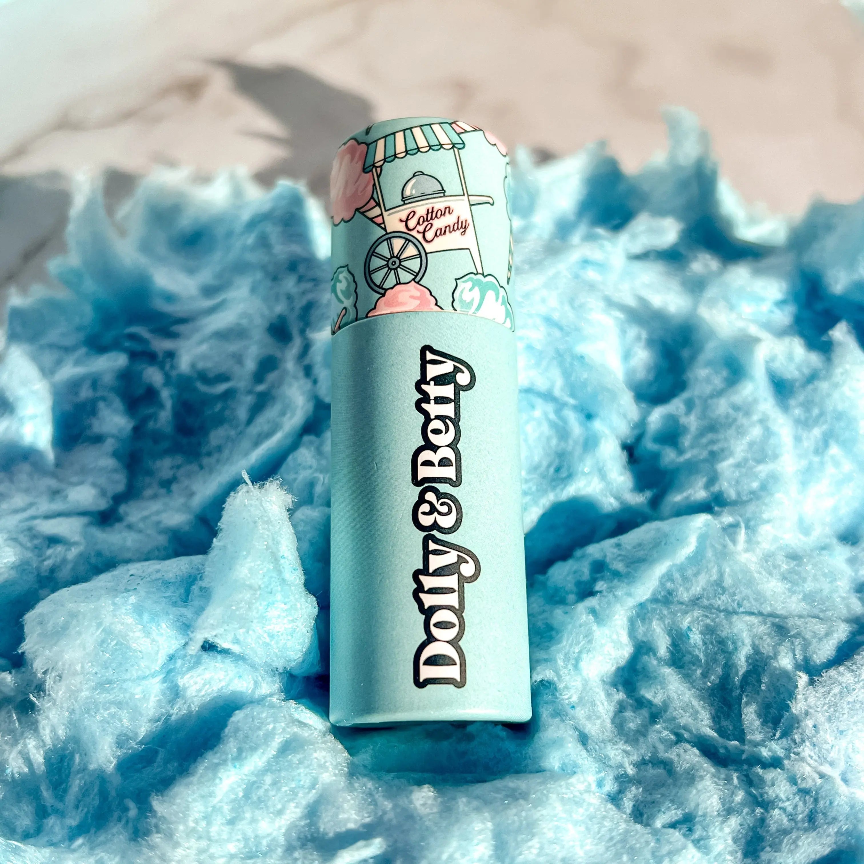 Lip balm with 'Dolly & Betty' branding on a blue cotton candy background